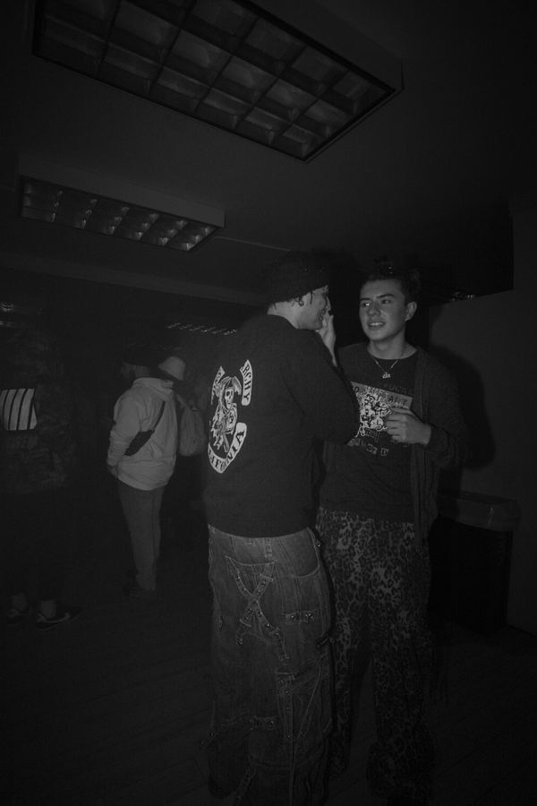 Two people talking in a dim room, one in leopard-print trousers.