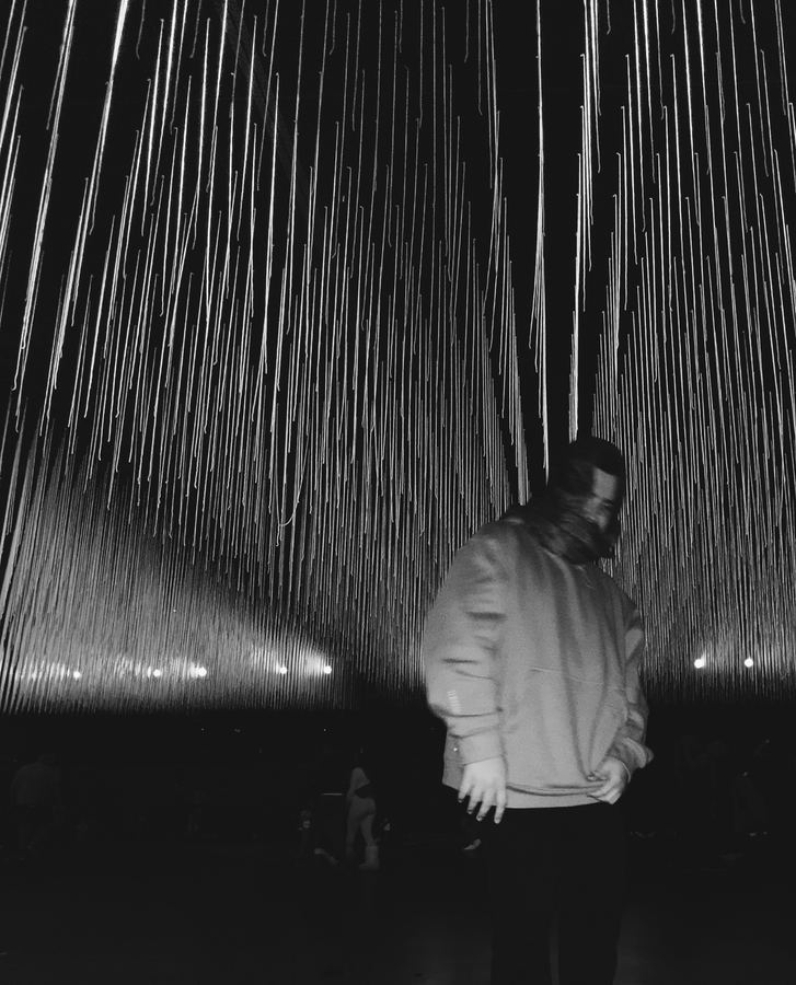 A figure in a sweatshirt beneath thousands of hanging white light strands.