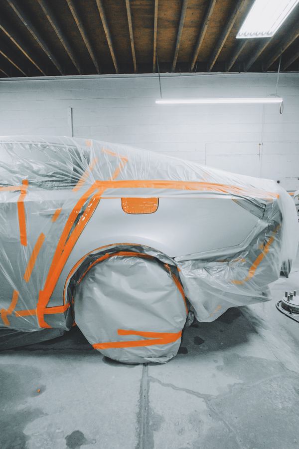 A car wrapped in plastic and orange tape in a paint booth.