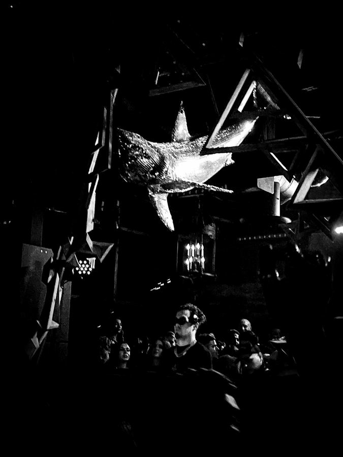 A mirror-tiled shark suspended above a crowd in black and white.