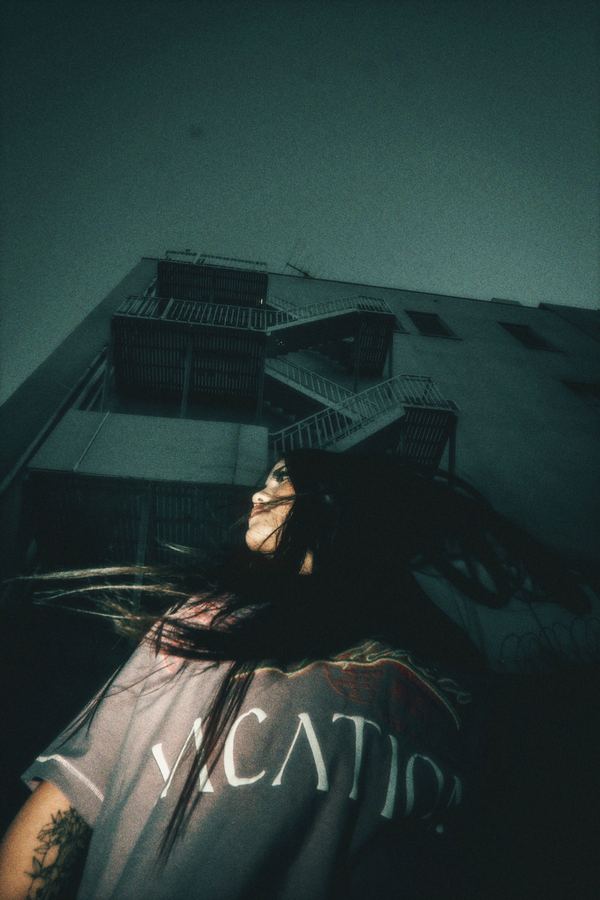 Looking up past someone with wind-blown hair at a building’s fire escape stairs.